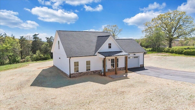 modern farmhouse featuring aphalt driveway, a standing seam roof, roof with shingles, metal roof, and stone siding