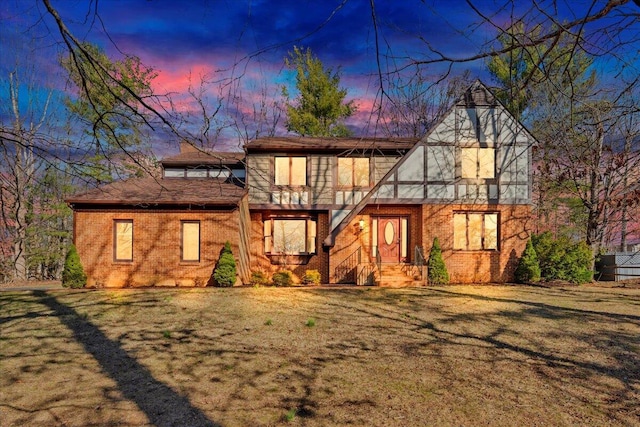 tudor home featuring brick siding, a chimney, and a yard