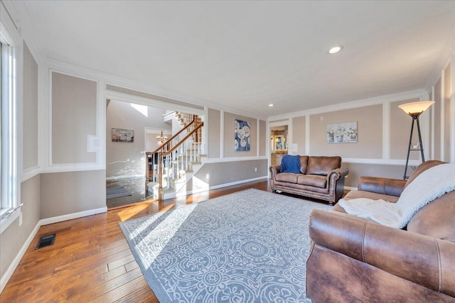 living area featuring baseboards, visible vents, stairs, hardwood / wood-style flooring, and crown molding