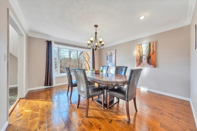 dining space with baseboards, wood-type flooring, an inviting chandelier, and crown molding