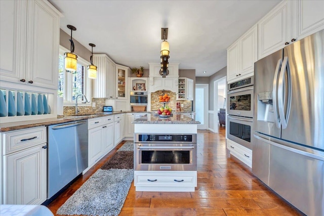 kitchen with wood finished floors, stainless steel appliances, white cabinets, decorative backsplash, and light stone countertops