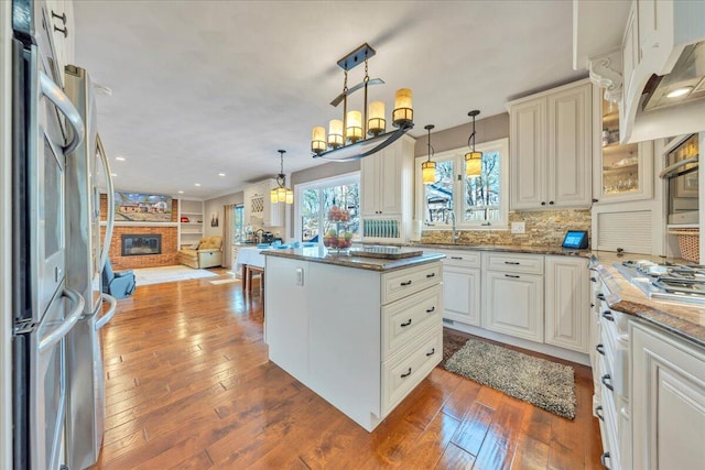 kitchen featuring a fireplace, open floor plan, wood-type flooring, fridge, and tasteful backsplash