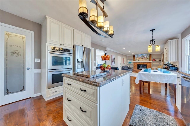 kitchen featuring dark wood-type flooring, decorative light fixtures, stone counters, appliances with stainless steel finishes, and a glass covered fireplace