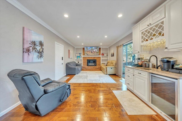 living area featuring a brick fireplace, crown molding, wine cooler, wet bar, and light wood-style floors