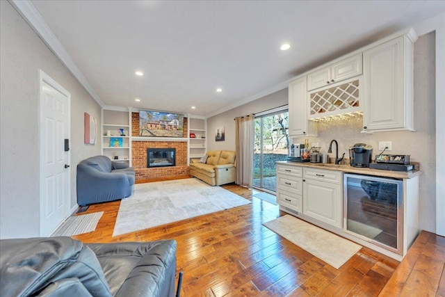 living room featuring indoor wet bar, a brick fireplace, beverage cooler, and light wood-type flooring