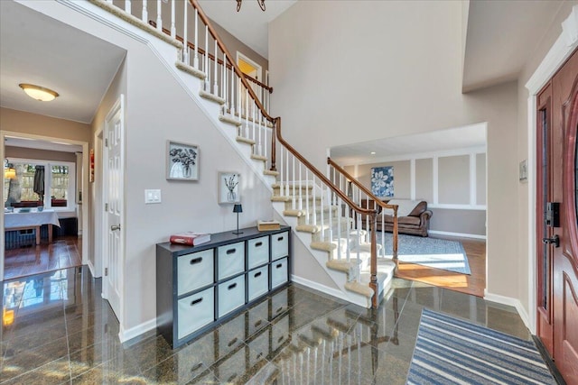 entrance foyer with stairs, granite finish floor, baseboards, and a towering ceiling