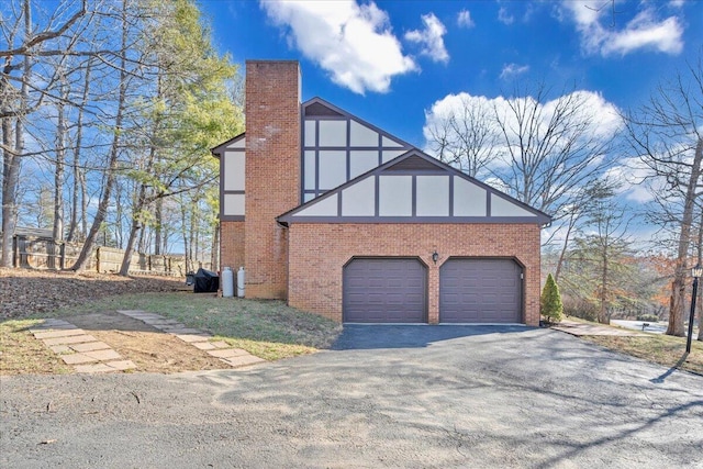 view of home's exterior with brick siding, driveway, a chimney, and an attached garage