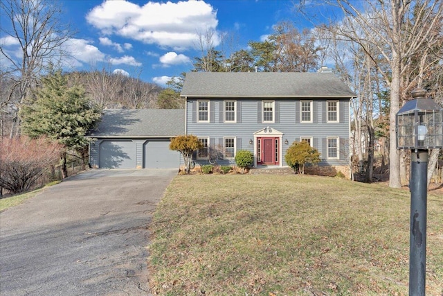 colonial home featuring a chimney, aphalt driveway, a front lawn, and an attached garage