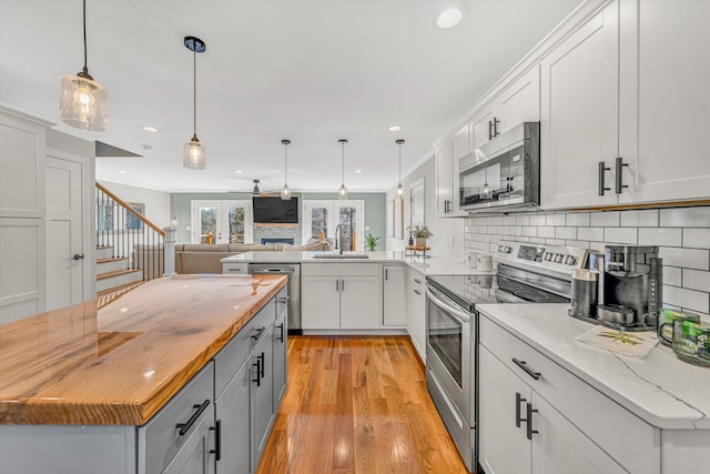 kitchen with butcher block counters, a sink, open floor plan, appliances with stainless steel finishes, and backsplash