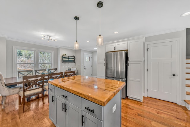 kitchen with a kitchen island, ornamental molding, freestanding refrigerator, light wood-style floors, and pendant lighting