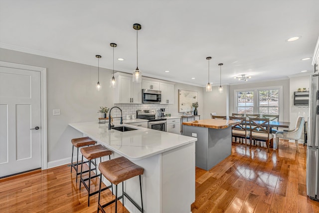 kitchen featuring ornamental molding, a center island, stainless steel appliances, light wood-type flooring, and a sink