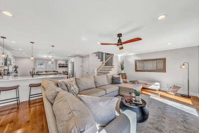 living area with recessed lighting, wood finished floors, a ceiling fan, stairs, and ornamental molding