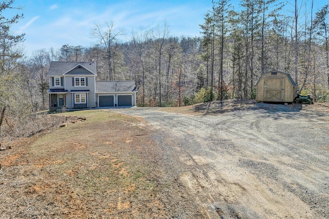 view of front of property featuring an outbuilding, a storage shed, a view of trees, a garage, and driveway