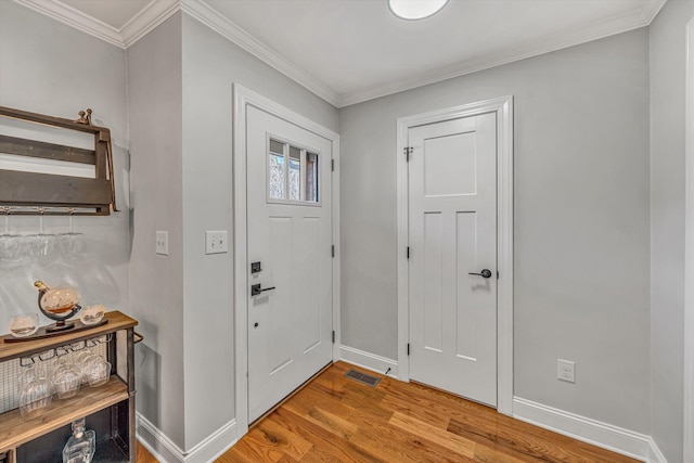 foyer with crown molding, visible vents, baseboards, and wood finished floors