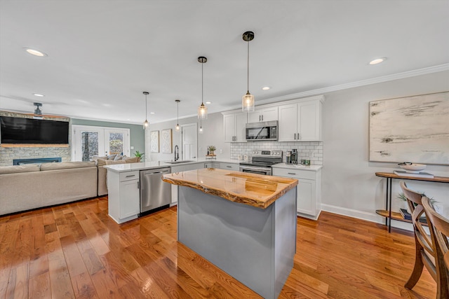 kitchen with light wood-style flooring, decorative backsplash, appliances with stainless steel finishes, a sink, and a peninsula