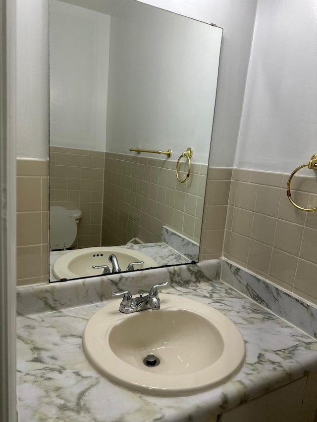 bathroom featuring toilet, wainscoting, tile walls, and vanity