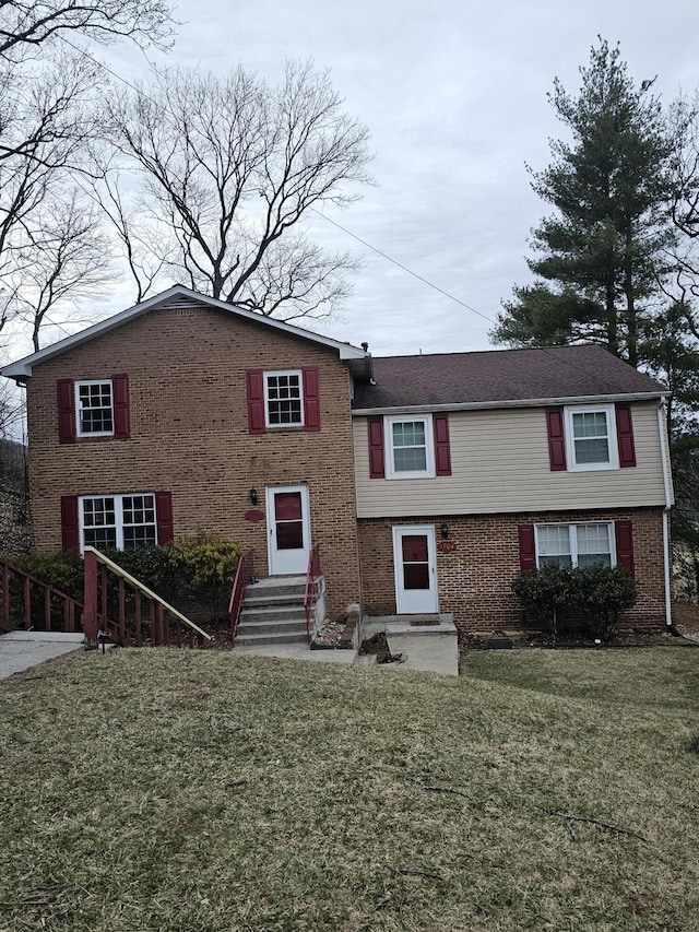 split level home featuring entry steps, a front yard, and brick siding