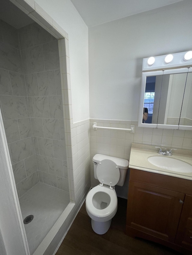 bathroom with a wainscoted wall, wood finished floors, vanity, tile walls, and a shower stall