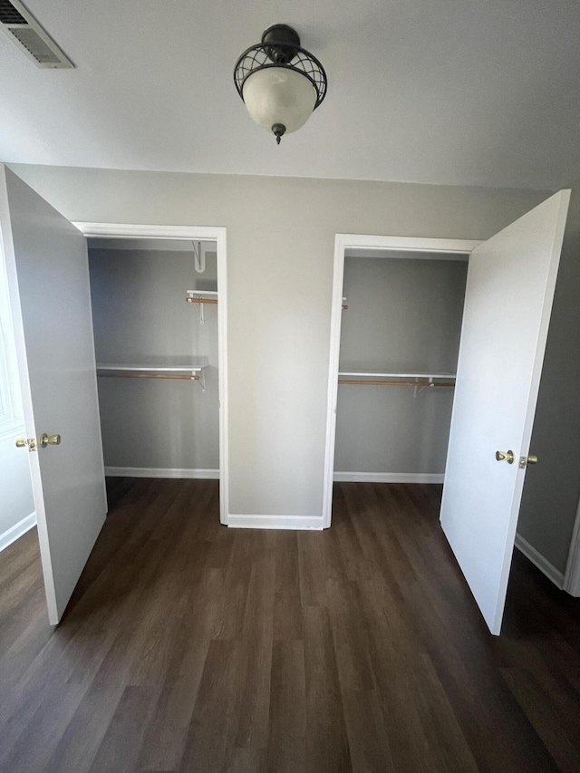 unfurnished bedroom featuring two closets, baseboards, visible vents, and wood finished floors