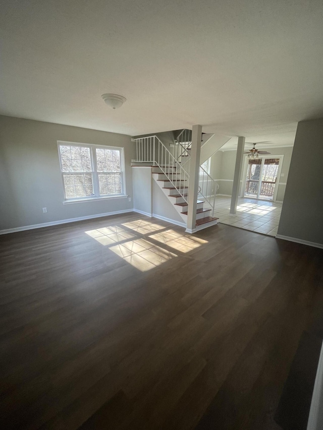 unfurnished living room featuring dark wood-type flooring, stairway, plenty of natural light, and baseboards