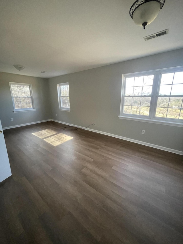 empty room featuring dark wood-style flooring, visible vents, and baseboards