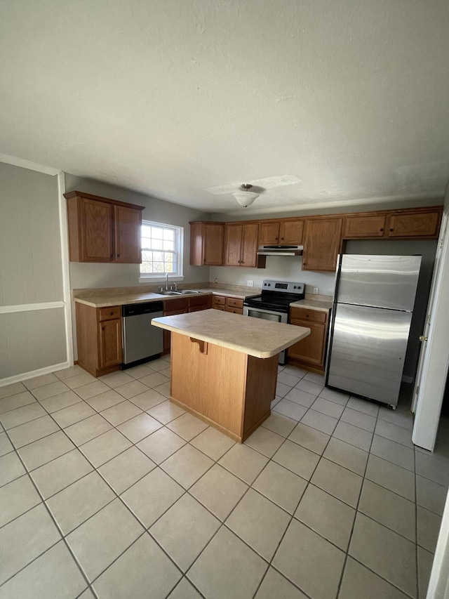 kitchen featuring light tile patterned floors, under cabinet range hood, stainless steel appliances, light countertops, and a center island