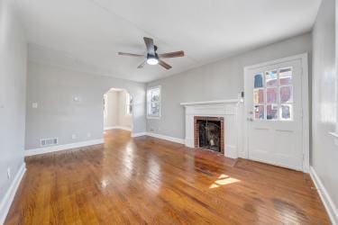 unfurnished living room featuring arched walkways, a fireplace, a ceiling fan, wood finished floors, and baseboards