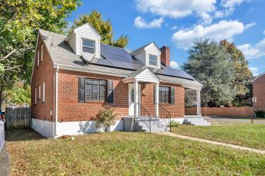 cape cod home featuring fence, a front lawn, solar panels, and brick siding