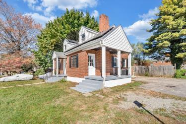 back of house with covered porch, a lawn, a chimney, and fence