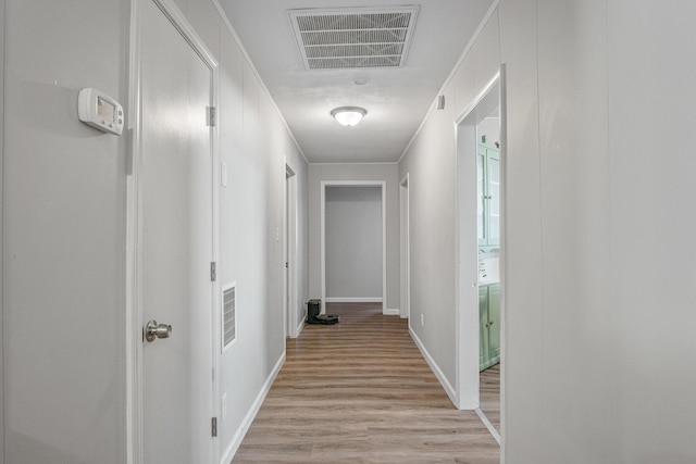 corridor featuring light wood-style floors, baseboards, visible vents, and crown molding