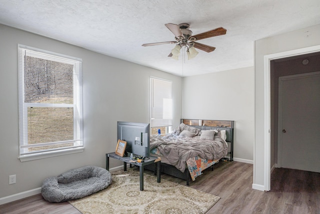 bedroom with a ceiling fan, a textured ceiling, baseboards, and wood finished floors