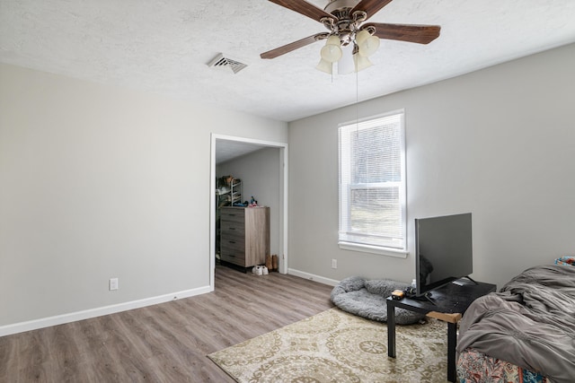 bedroom featuring a textured ceiling, ceiling fan, wood finished floors, visible vents, and baseboards