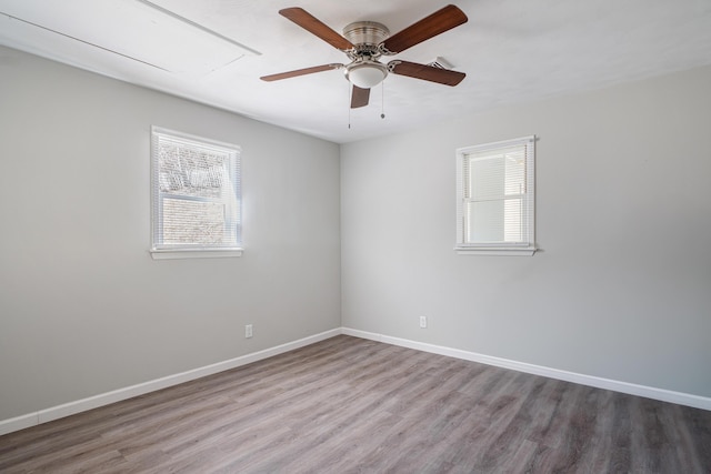 empty room featuring attic access, a ceiling fan, baseboards, and wood finished floors