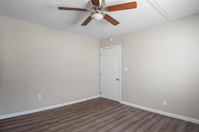 empty room featuring dark wood-style floors, attic access, baseboards, and a ceiling fan