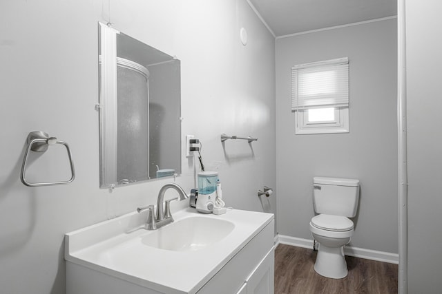 bathroom featuring toilet, wood finished floors, vanity, baseboards, and crown molding