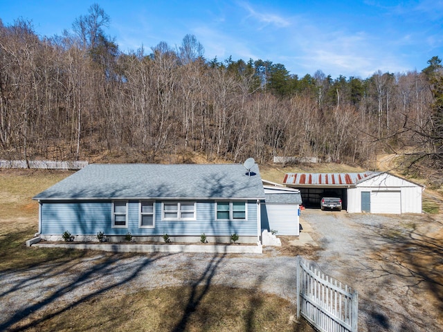 view of front of home featuring an outbuilding, dirt driveway, a shingled roof, fence, and a garage