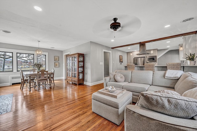 living area featuring visible vents, ceiling fan with notable chandelier, baseboards, and light wood finished floors