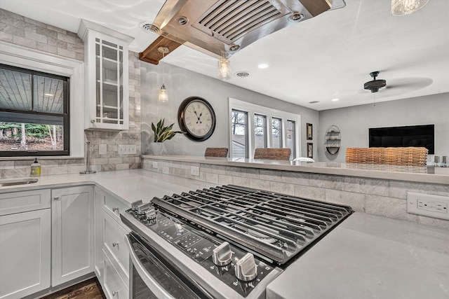 kitchen with visible vents, stainless steel range with gas stovetop, light countertops, glass insert cabinets, and tasteful backsplash