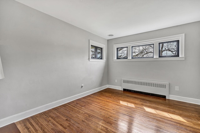 spare room with radiator, wood finished floors, and baseboards