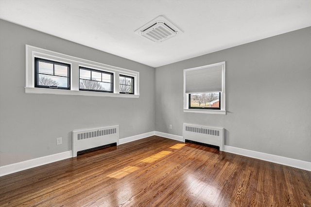 empty room featuring hardwood / wood-style floors, radiator, and visible vents