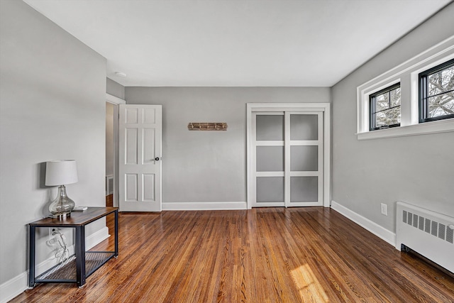 empty room featuring baseboards, wood finished floors, and radiator heating unit