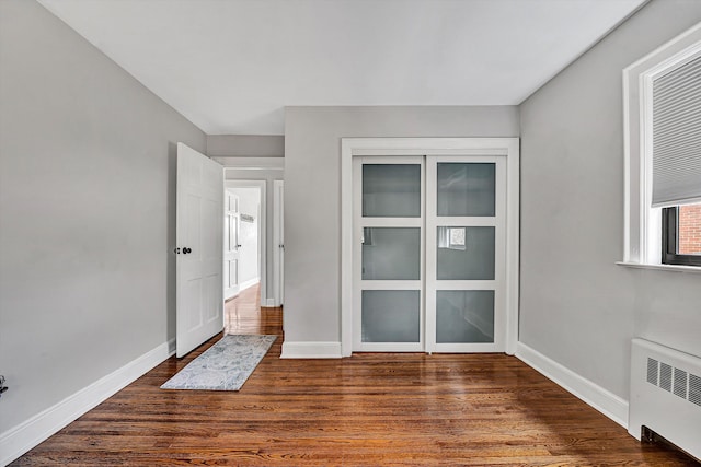 spare room featuring baseboards, dark wood-type flooring, and radiator