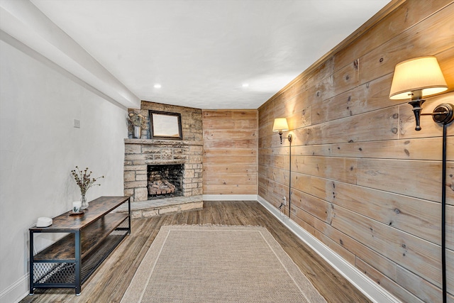 unfurnished living room featuring baseboards, wood finished floors, a fireplace, and wood walls