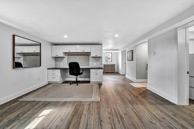 unfurnished office with built in desk, recessed lighting, baseboards, and dark wood-style flooring