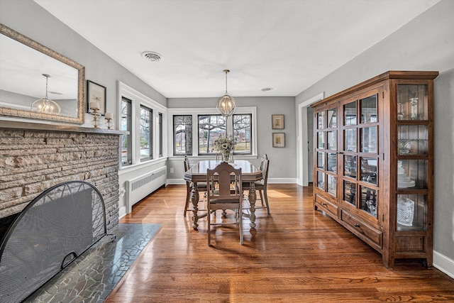 dining room with visible vents, a fireplace with flush hearth, a notable chandelier, wood finished floors, and radiator heating unit