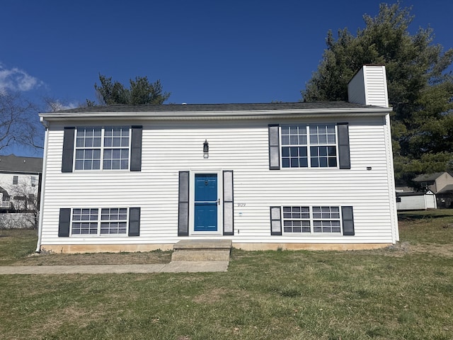 raised ranch with entry steps, a chimney, and a front lawn