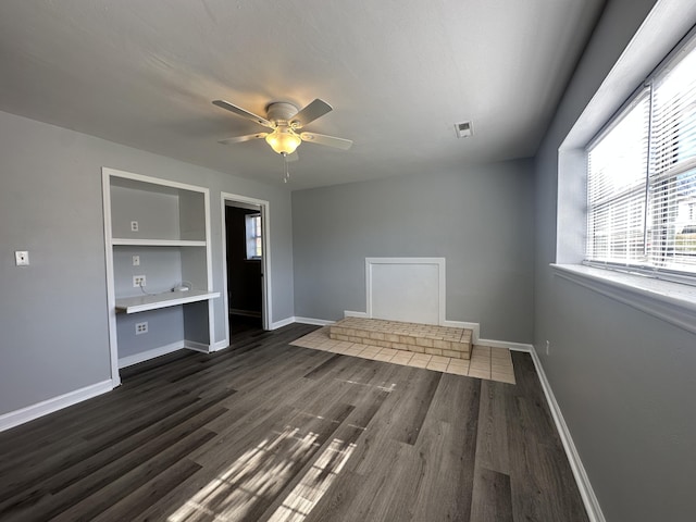 interior space featuring dark wood-style flooring, built in desk, visible vents, a ceiling fan, and baseboards