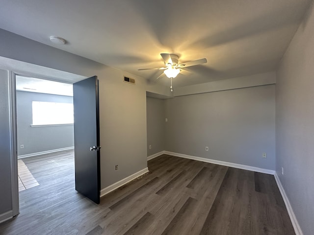 unfurnished room featuring a ceiling fan, dark wood-style flooring, visible vents, and baseboards