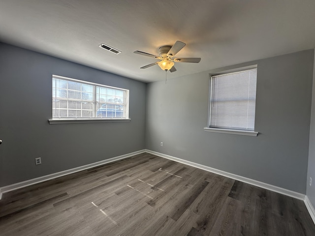 empty room with a ceiling fan, visible vents, dark wood finished floors, and baseboards