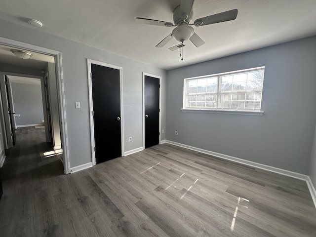 unfurnished bedroom with dark wood-style flooring, visible vents, ceiling fan, and baseboards